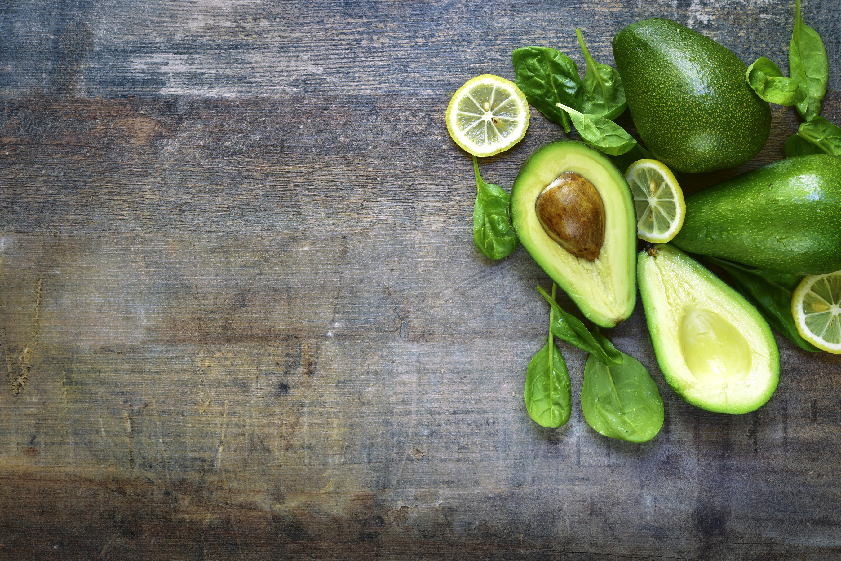 Ripe fresh organic avocado with spinach leaves and lemon slices.